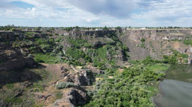 Bulutlu gökyüzünün altındaki tepeler ve uçurumlarla çevrili küçük bir göl manzarası.