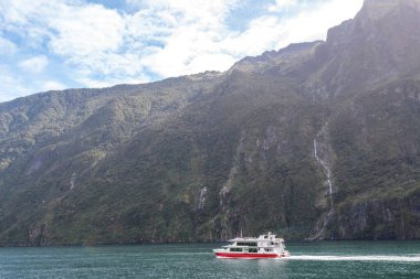 Yeni Zelanda 'nın Güney Adası' ndaki Milford Sound Fiord 'da şelalenin yanında küçük bir gemi.