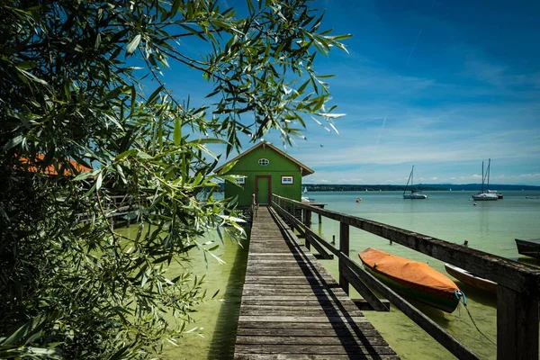 青い空に対して緑の湖の家につながる小さな木製の橋 — ストック写真
