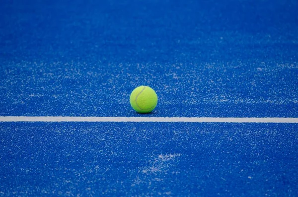 paddle tennis ball on the line of a blue paddle tennis court