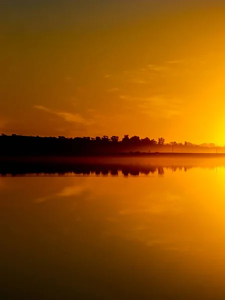 日落时带着树木和天空倒映在水面上的平静湖景 — 图库照片
