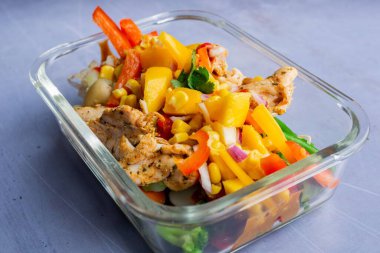 Şeffaf bir tabakta tavuk, patates ve çiğ sebze.