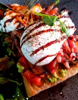 Avokado soslu, domatesli ve balzamik soslu haşlanmış yumurtalı tostun dikey yakın çekimi.