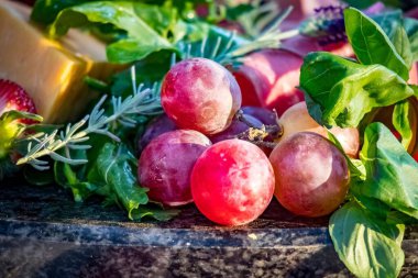 Taş tabakta bir yığın üzüm, peynir ve taze otlar.