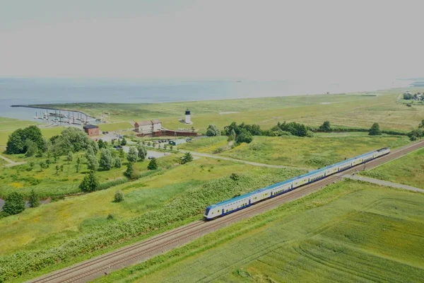 A scenic view of a modern train in a rural area surrounded by green fields