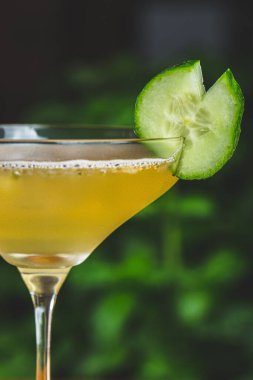 Bir parça salatalıkla servis edilen ferahlatıcı bir kokteylin dikey çekimi.