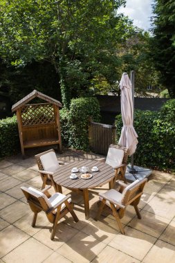 Parktaki rahat bir köşenin dikey çekimi. Tahta sandalyeler ve kahvaltı için masa.