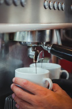 Kahve makinesinin altında kahve fincanı tutan bir barmen.
