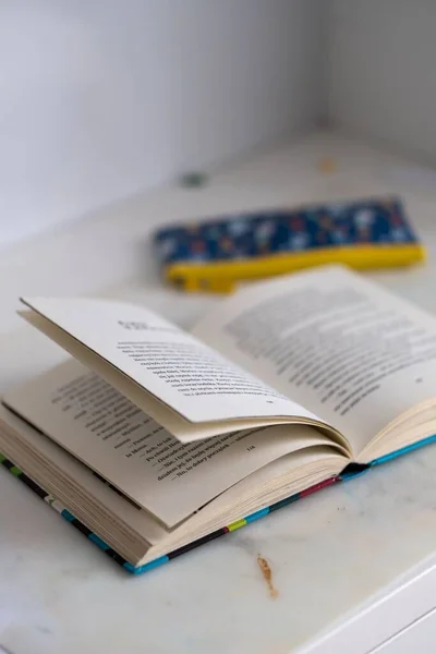 白桌子上的一本打开的故事书和一个铅笔盒的垂直视图 — 图库照片