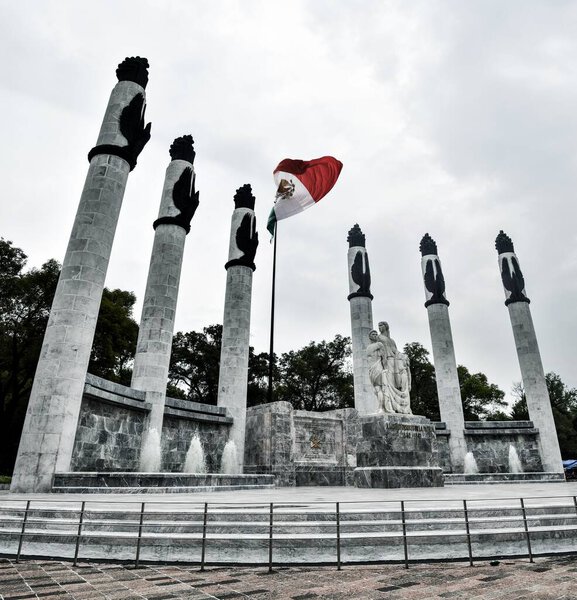 Живописный вид на флаг Мексики, окруженный колоннами на облачном фоне неба