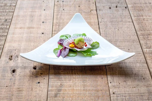 一个美味的扇贝开胃菜在贝壳与草药在三角白盘上 — 图库照片