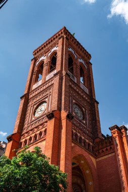 Güneşli bir günde kırmızı tuğlalardan yapılmış bir saat kulesi.