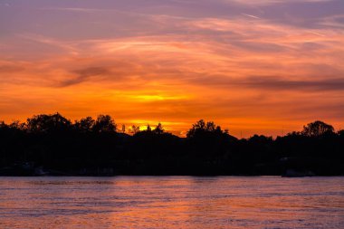 Gün batımında arka planda ağaçlar olan bir göl.