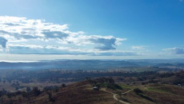 Mavi parlak gökyüzünün altında büyüyen ağaçlarla çevrili bir dağ manzarası.
