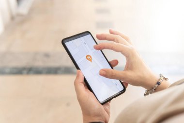 Akıllı telefonlu bir kadın şehrin haritasında restoranları, ilgi alanlarını ve toplu taşıma araçlarını arıyor. Çeşitli simgeler
