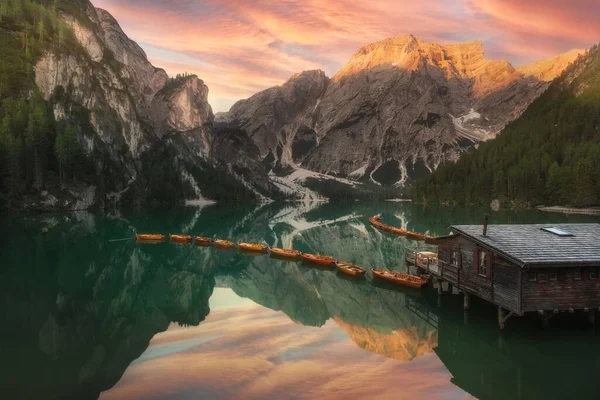 日没時には山や森に囲まれた木製のボートの行を持つ湖の素晴らしいショット — ストック写真