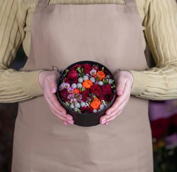 A faceless florist in apron holding small colorful flowers in round black box