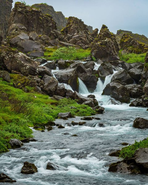 A vertical shot of a river flowing in a rural area surrounded by rocks and grass in Iceland