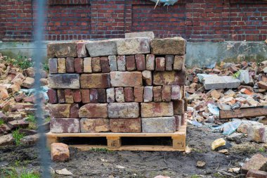 Yıkılan bir binanın arka planına karşı istiflenmiş tuğla yığını