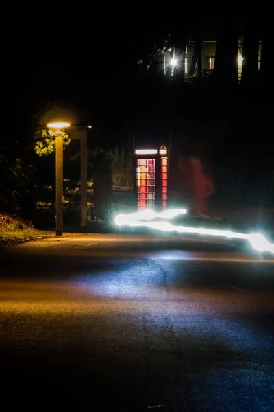 A vertical shot of a dark street and a light trail passing by a telephone booth at Center Parcs Woburn