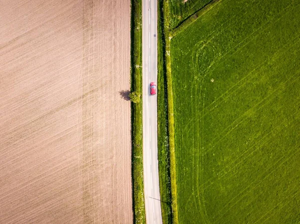 晴れた日に田舎の農地に沿って運転する赤い車の空中ドローンの眺め — ストック写真