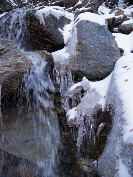 一道流过白雪岩石的瀑布的垂直镜头 — 图库照片