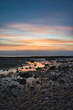 Gün batımında dalgalı kumla dalgalı bir sahilin dikey görüntüsü.