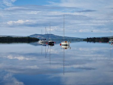İskoçya 'da bulutlu bir günde Loman Gölü' nde yelken açan teknelerin manzarası