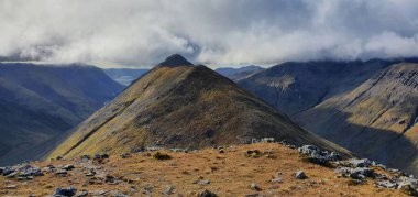 Bulutlu gökyüzünün altında büyüleyici bir dağ manzarası