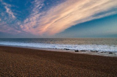 Gün batımında kumlu bir sahile vuran dalgaların manzarası çizgili bir gökyüzüyle
