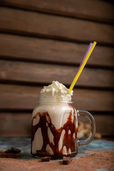 A milkshake with chocolate syrup on a gray marble table with chocolate