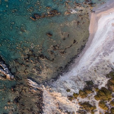 Yunanistan 'da yeşilliklerle kaplı kayalık bir sahilin yakınındaki turkuaz bir denizin havadan görünüşü