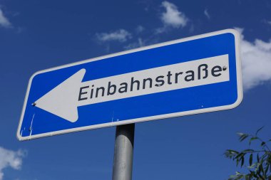 Trafik levhası tek yönlü bir yol olduğunu gösteriyor. Mavi yazlık gökyüzünün önündeki bulutlu mavi işaret. Alman trafik levhası 220-10.