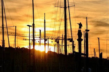 Rıhtımda duran bir adamın heykeli. Yelkenli gemilerin direkleriyle çevrili.