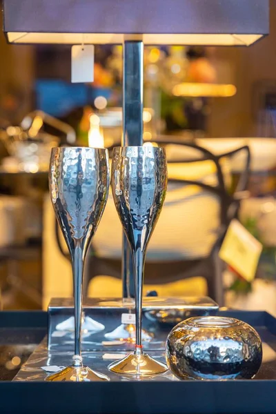 Bir kafede lambanın altında gümüş bardakların dikey yakın çekimi.