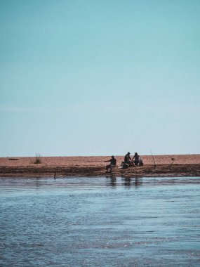 Güneşli bir günde gölün kıyısında oturan ve balık tutan üç adamın dikey çekimi.