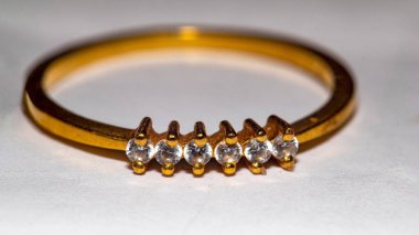 Beyaz bir yüzey üzerinde bir sıra elmasla ince altın bir yüzüğün yakın plan çekimi.