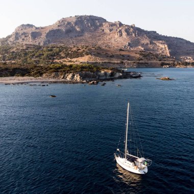 Yunanistan 'da kayalık bir sahil kenarında turkuaz bir denizde yüzen bir teknenin havadan görüntüsü