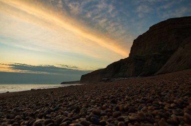 Gün batımında deniz kenarında çizgili pembe gökyüzü olan bir kaya oluşumunun alçak açılı görüntüsü.