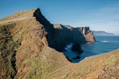 Bulutlu arka planda tepelerle çevrili mavi bir deniz manzarası