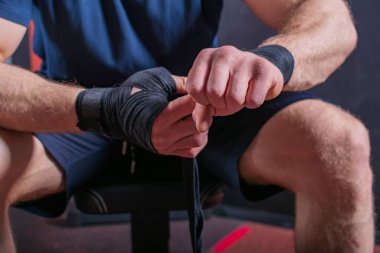 Kanepeye oturup bileğini düzeltmek için elastik bandaj saran genç ve güçlü dövüş sanatçısının kesilmiş vücudu..