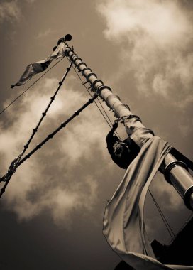 Üzerinde Nishan Sahib bayrağı olan bir direğin alçak açılı görüntüsü tek renkli bulutlu gökyüzü fotoğrafına karşı.