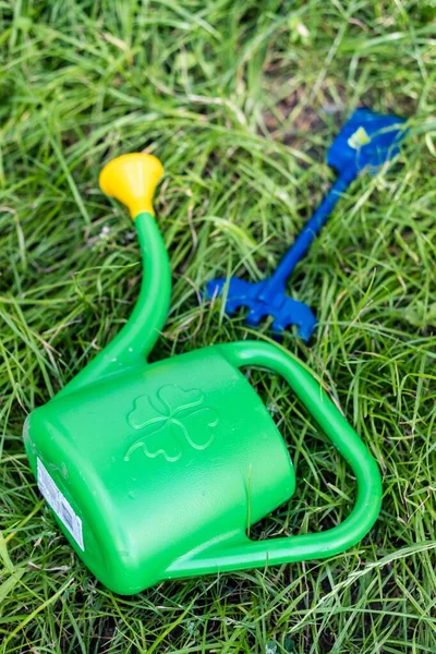 A green plastic watering can laying on fresh grass