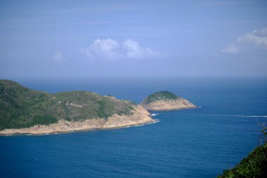 Bulutlu bir gökyüzünün altındaki mavi denize karşı yeşil bir manzaranın kuş bakışı görüntüsü.
