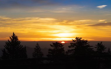 Kırsal bölgedeki bulutlu gökyüzünde canlı bir günbatımının manzarası.