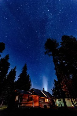 Buzul Ulusal Parkı yakınlarındaki Düz Kafalı Ulusal Orman 'daki ahşap kulübenin alçak açılı görüntüsü yıldızlı gökyüzü arka planına karşı.