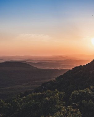 Orman tepelerinin üzerinde güzel bir günbatımının dikey görüntüsü.
