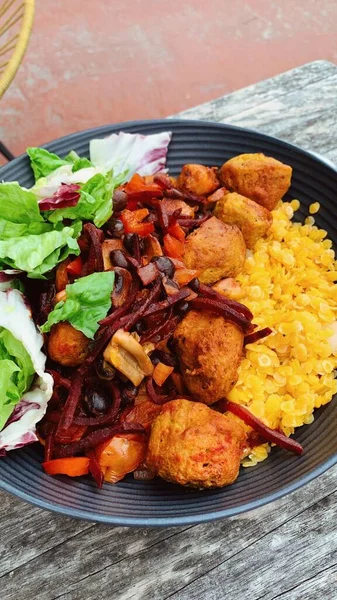 A vertical closeup of a vegan meal with red lentils, soy meatballs, beetroot, and other vegetables