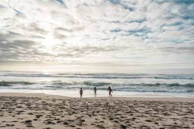 Üç çocuk açık bulutlu bir günde Portekiz plajında oynuyorlar.