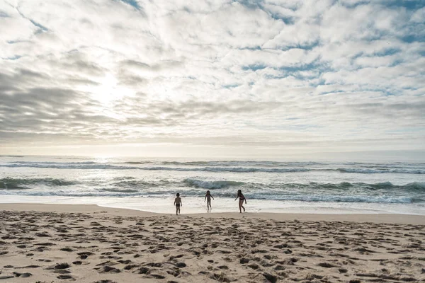 Üç çocuk açık bulutlu bir günde Portekiz plajında oynuyorlar.